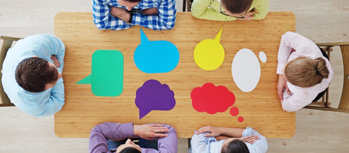 Team of business people in casual clothes sitting around the table with paper dialog boxes, discussing opinion concept